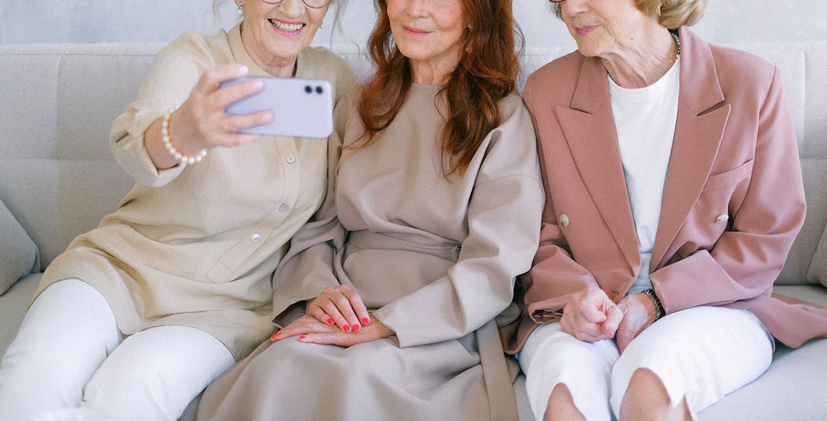 ソファに腰かけてスマートフォンで自撮りする3人のシニア女性